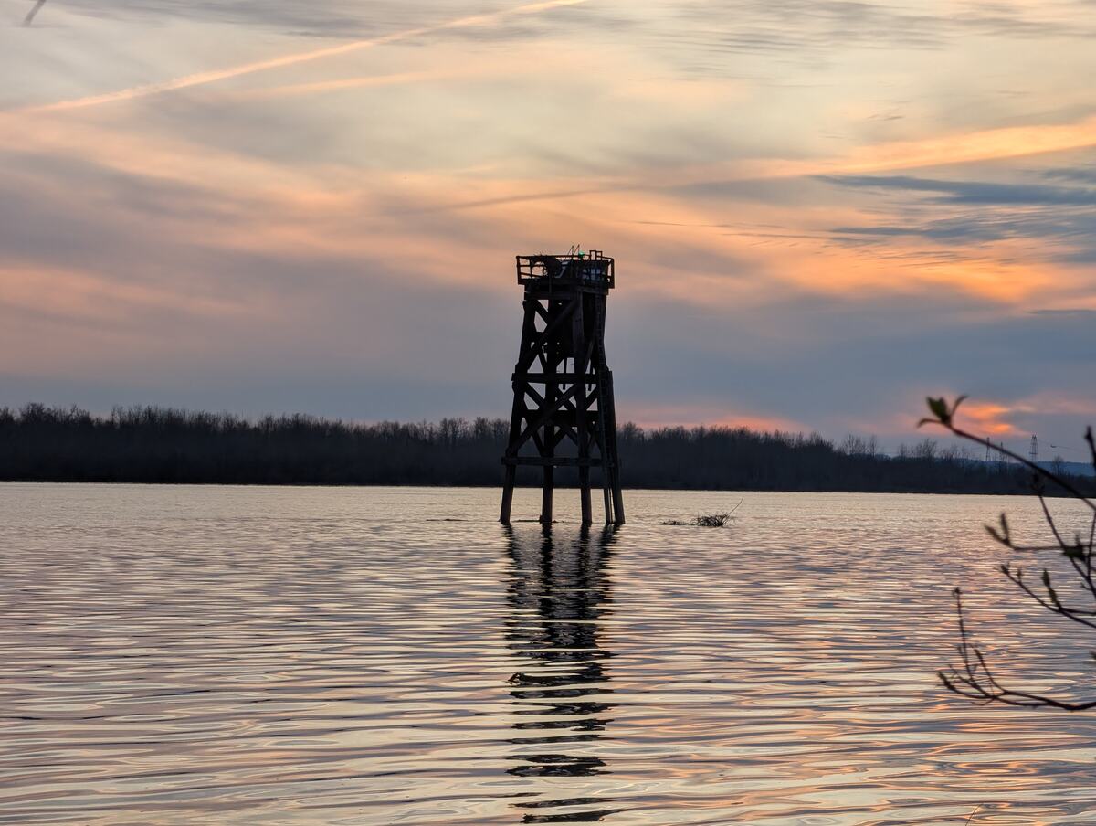 A weathered wooden channel-marker tower silhouetted on calm water at dusk