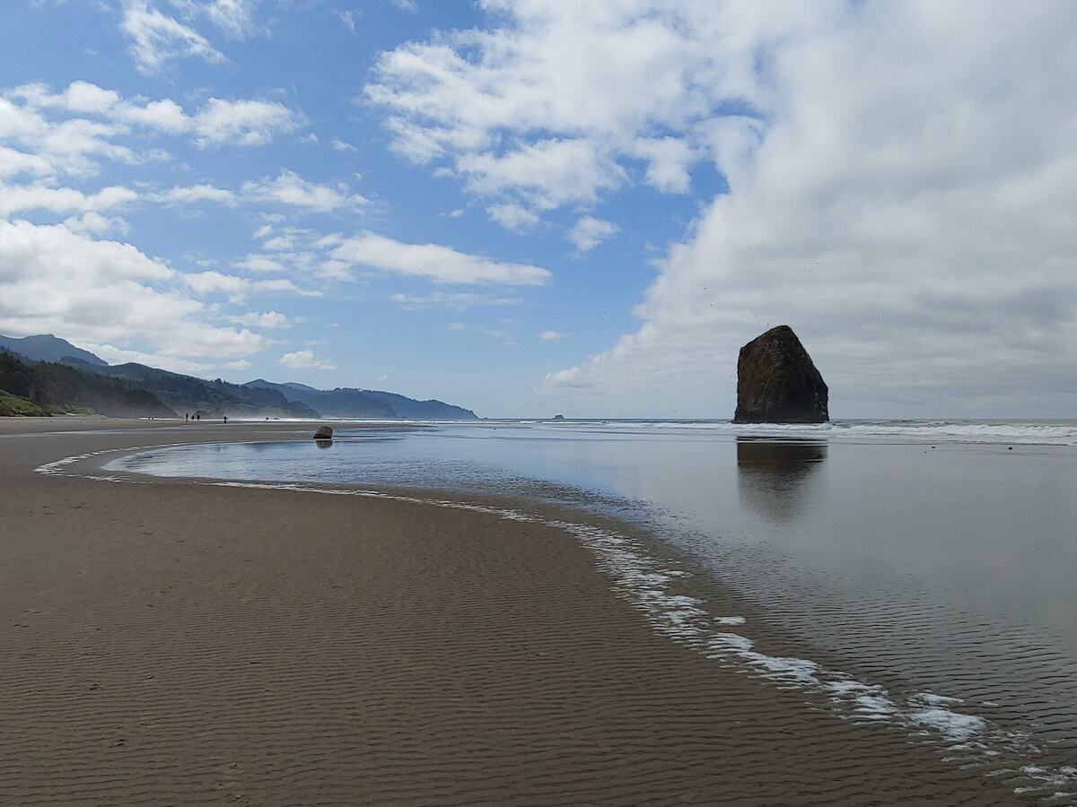 A tall sea stack on a wide sandy beach at low tide under a bright blue sky