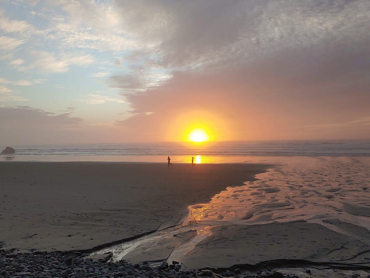 The sun setting on the horizon over a beach with wet-sand reflections