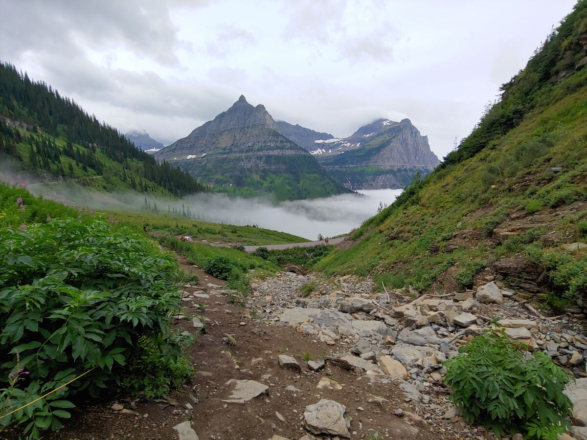Jagged mountain peaks above a green valley filled with low morning fog, Glacier National Park