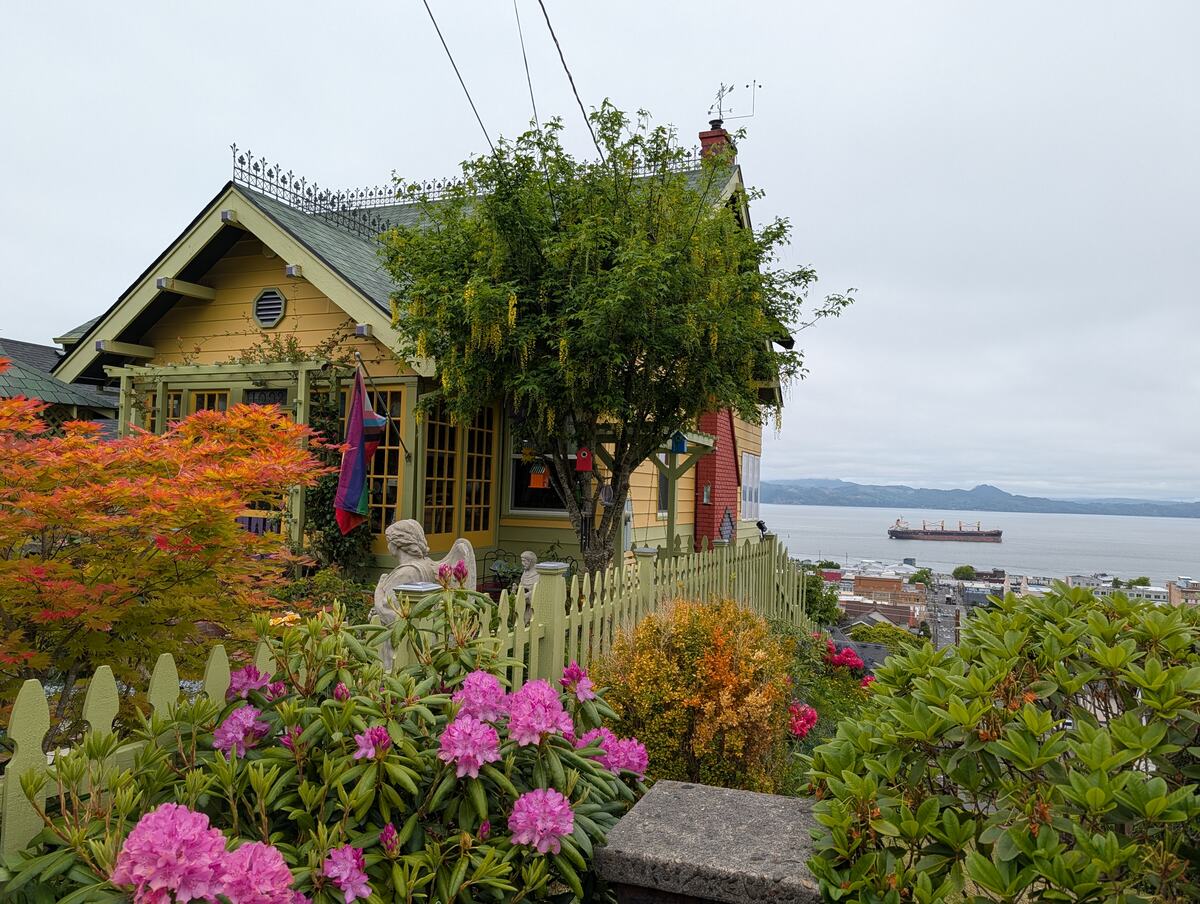 Colorful yellow Victorian house with a flower garden overlooking a harbor with a cargo ship