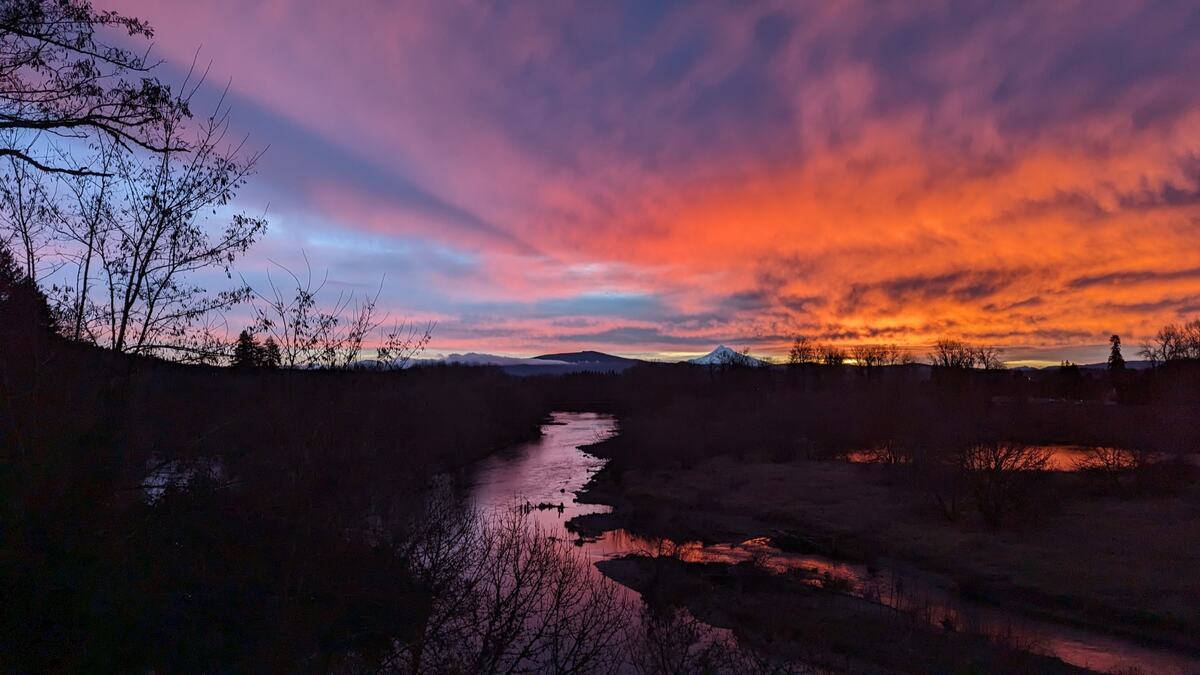 Vivid orange and purple sunrise sky over a river, with Mount Hood on the western horizon