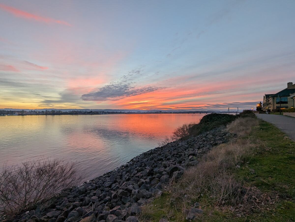 Pink and orange sunset over a river with a rocky path along the shore