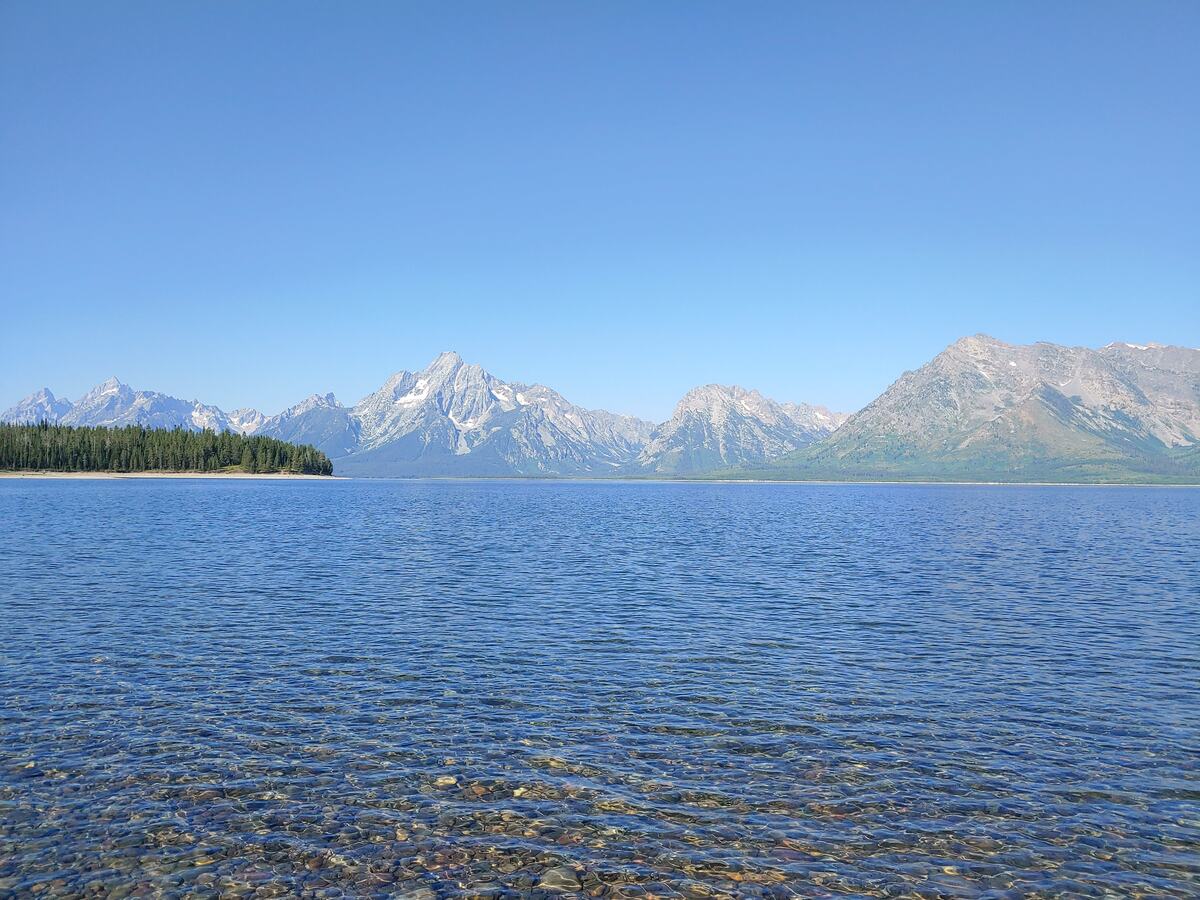 Snow-streaked Teton peaks across a calm, clear blue lake