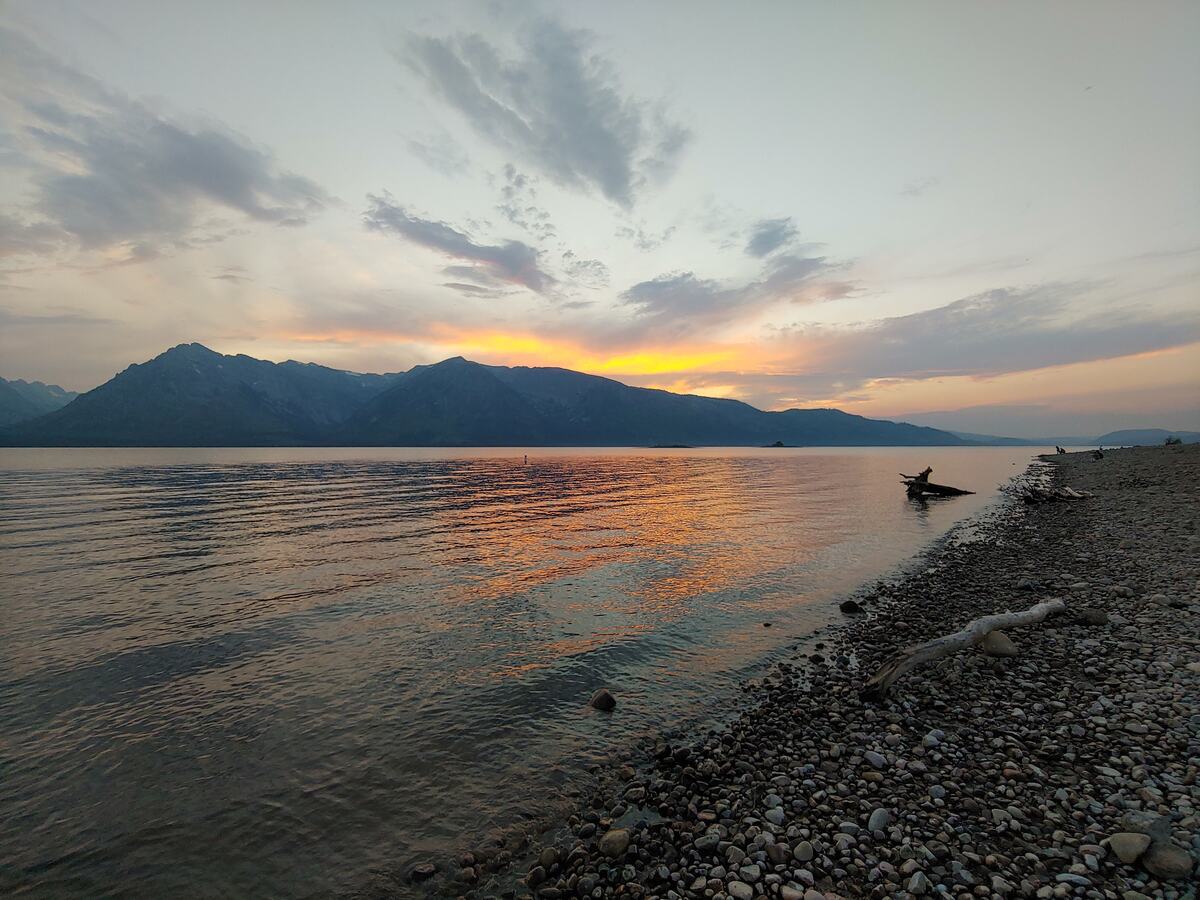 Pebble beach and driftwood along a lake at sunset with mountains in silhouette