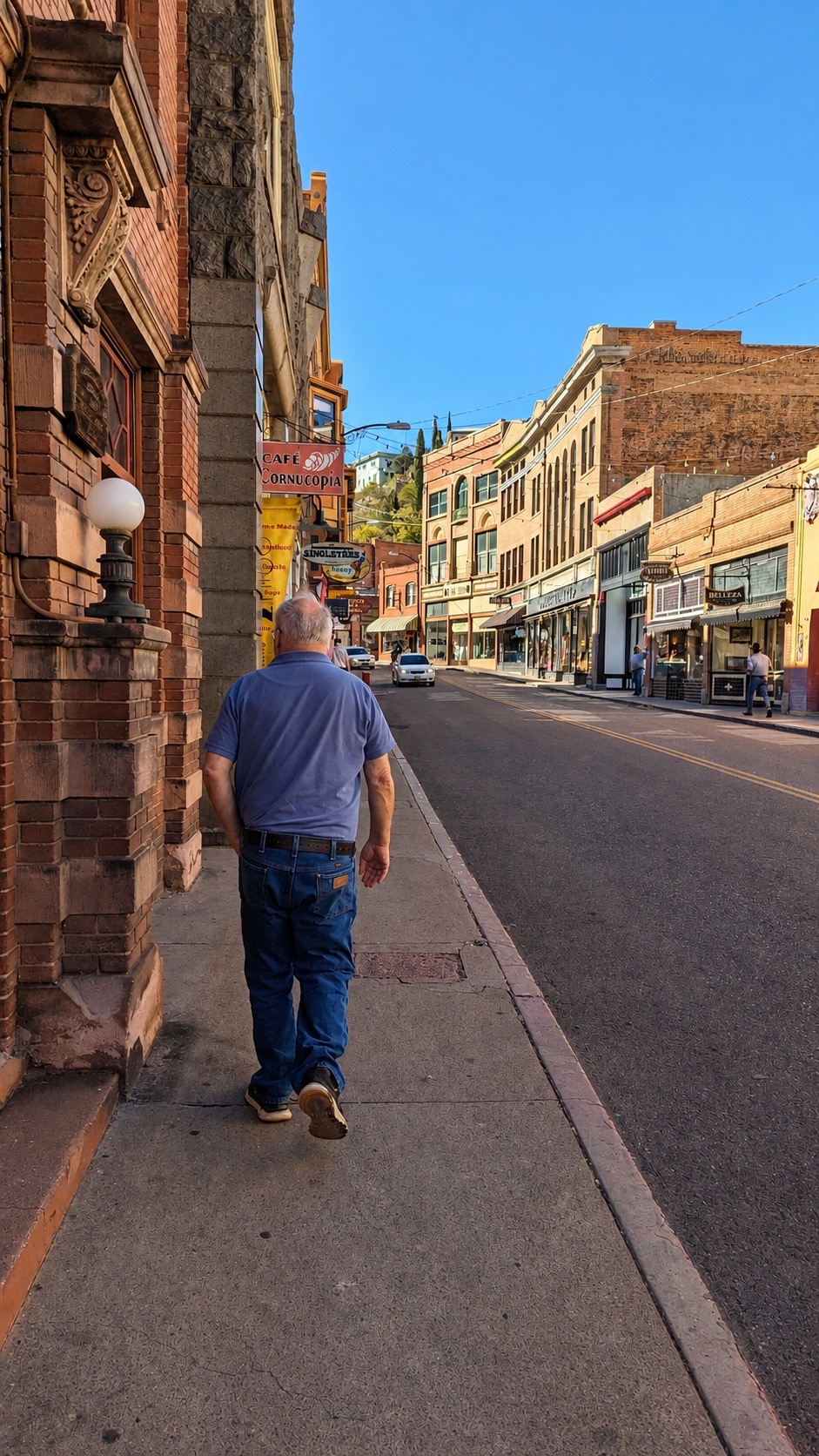 Mike walking up the sidewalk of Bisbee's historic downtown, brick storefronts glowing in the sun.