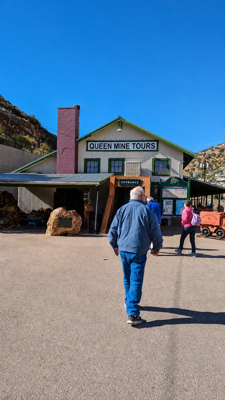 Mike walking toward the Queen Mine Tours building under a deep blue Arizona sky.
