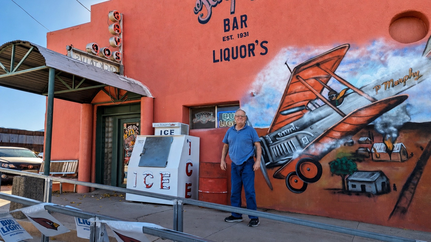 Mike standing by a biplane mural on the coral-pink wall of a 1931 bar in Bisbee.