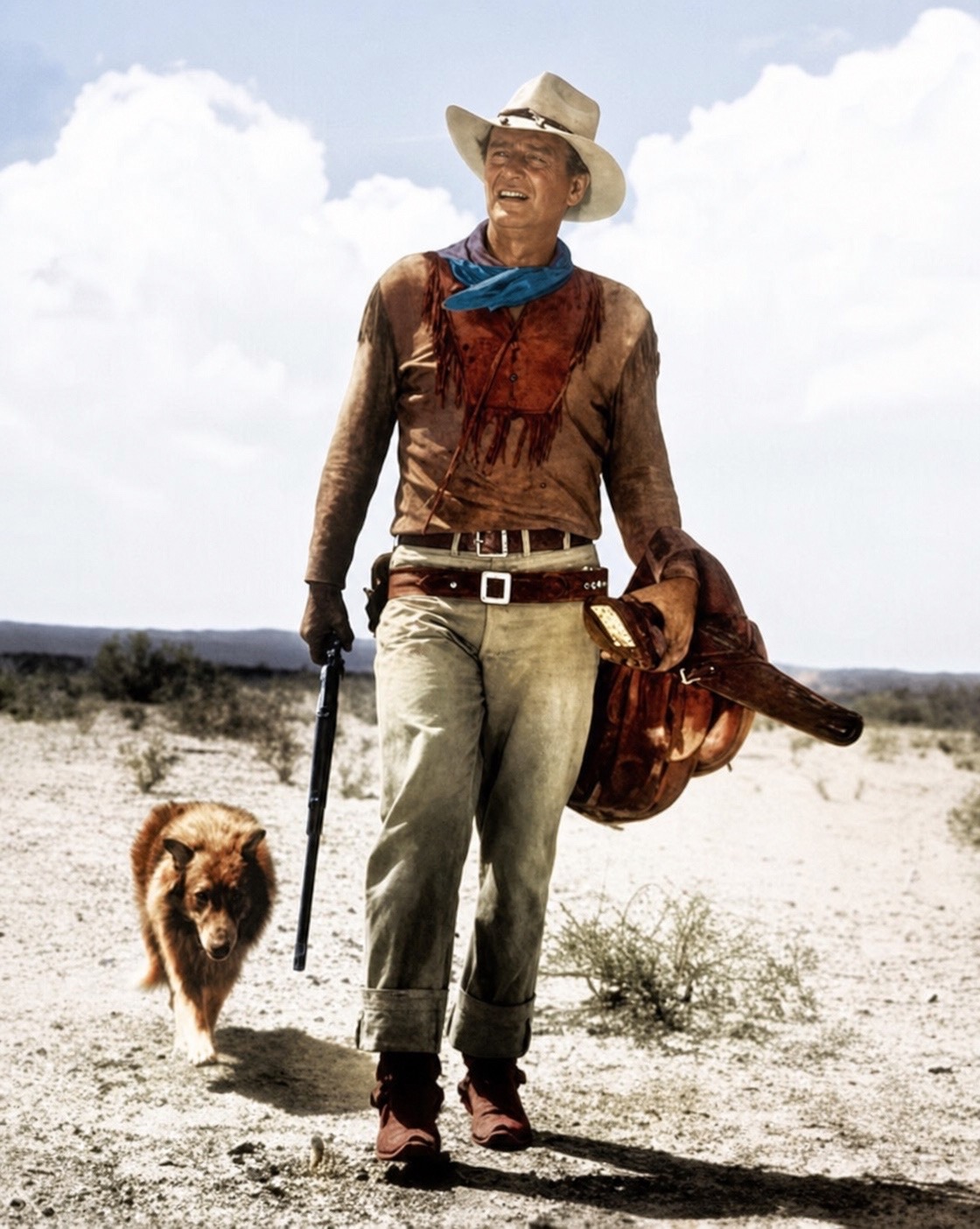 John Wayne walking through the desert carrying a saddle, a dog trotting beside him. Restored color still.