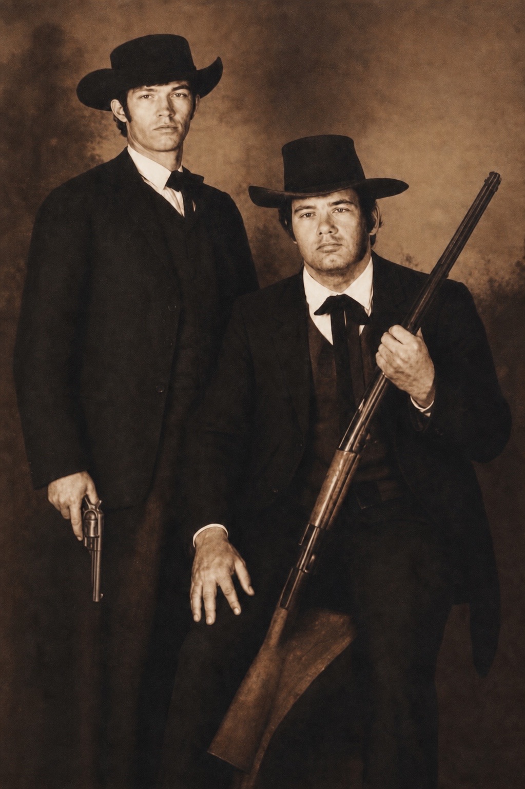 Sepia old-time studio portrait of Mike Anderson and his friend Stoddard in frontier suits and broad black hats, Mike seated holding a rifle.